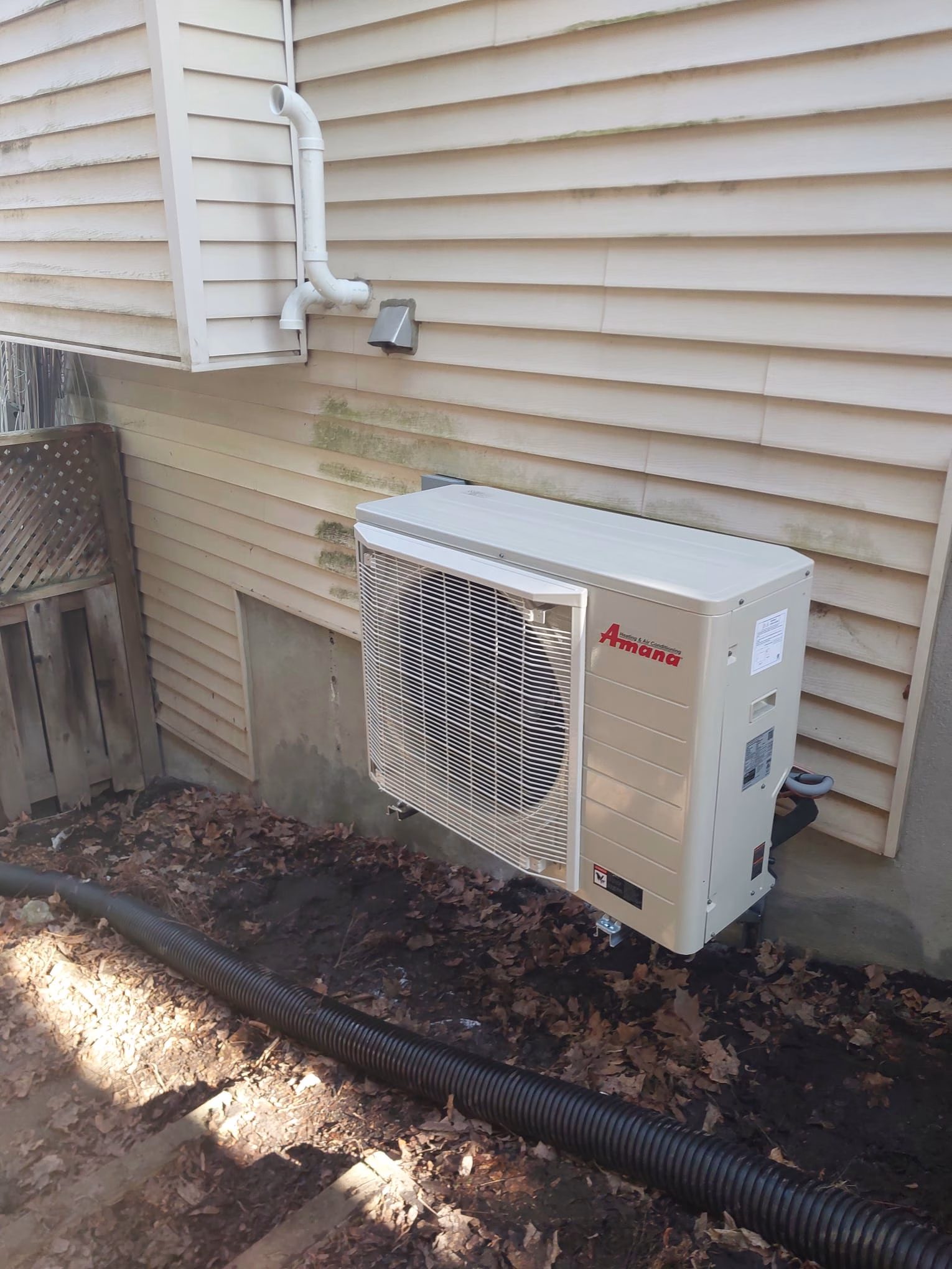Amana outdoor heat pump installed beside light-coloured siding.
